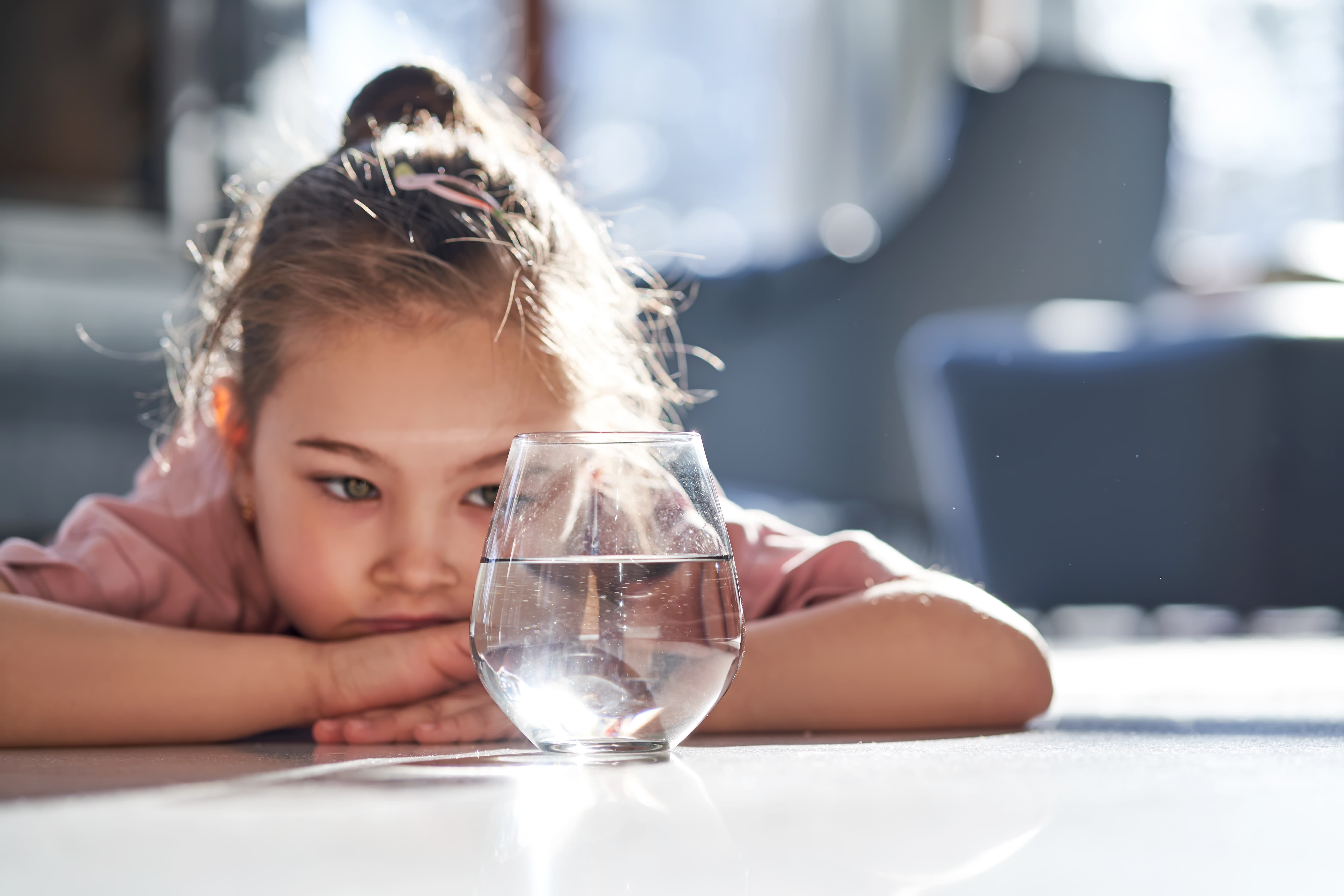 A small child looking at a glass of water.
