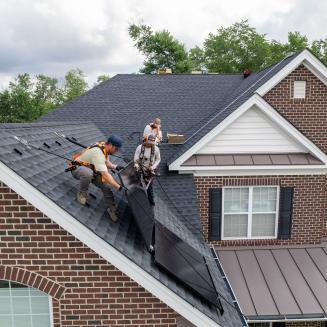 Workers installing solar panels on roof of suburban house