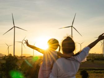 Woman and child with arms extended look at wind turbines as the sun sets