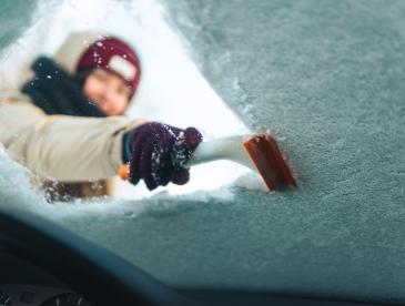 Woman cleans windshield with ice scraper