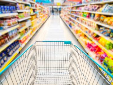 A shopping cart going down a colorful aisle at the grocery store.