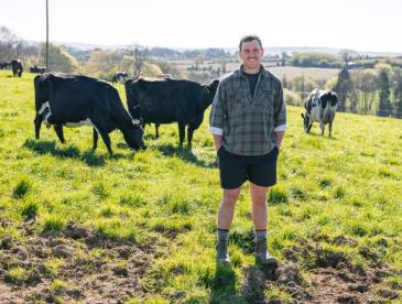 Dairy farmer, with green pasture and cows in the background.