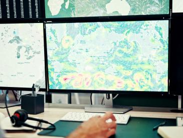 Four computer screens showing various maps and data.