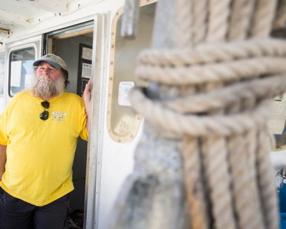 Keith “Buddy” Guindon standing at the door to a fishing boat with a rope tied up in the foreground