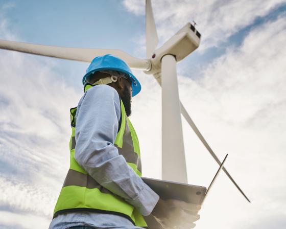 Worker in bright blue hard hat standing beneath a wind turbine.